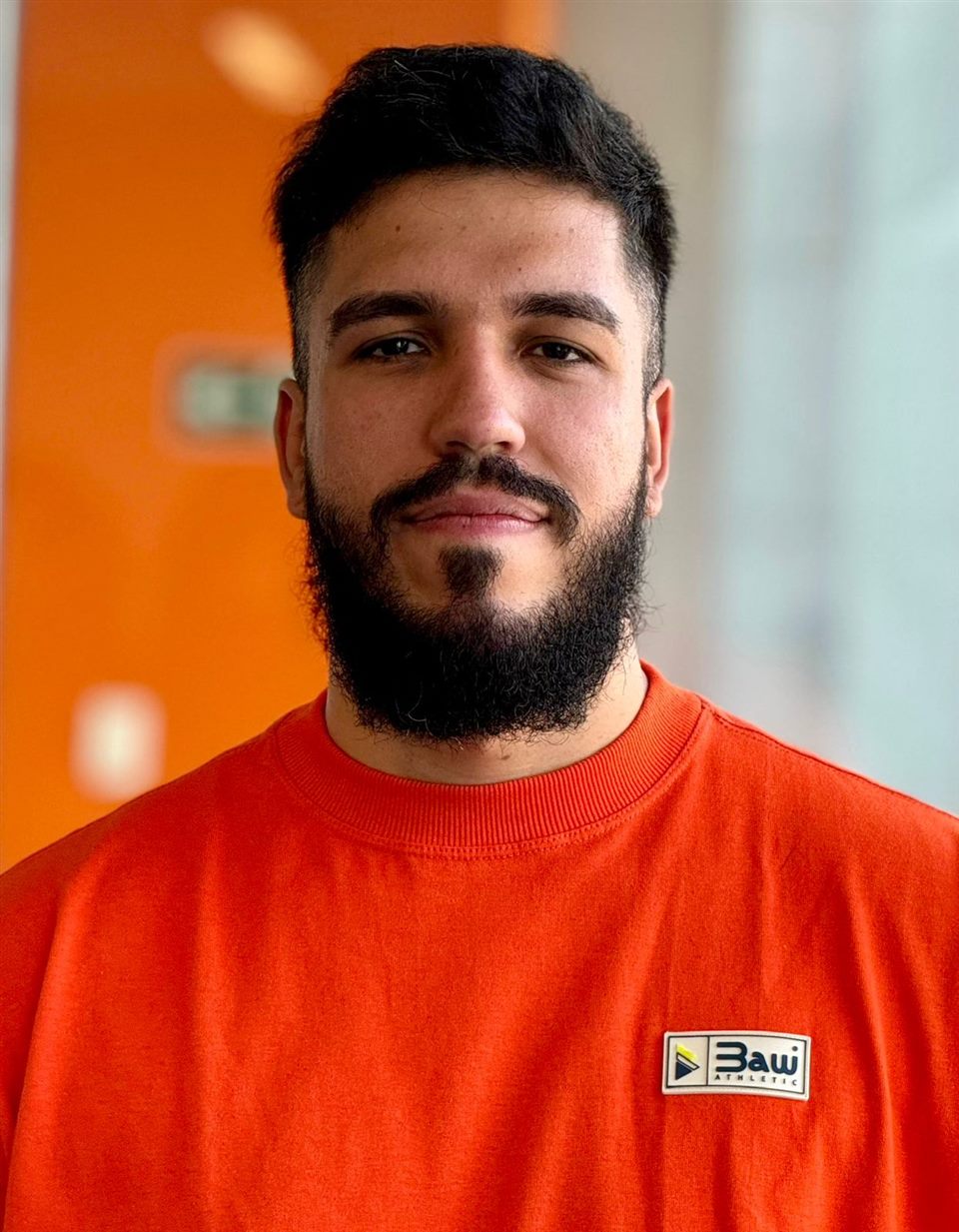 Valbert Junior, sorrindo levemente, de camiseta laranja